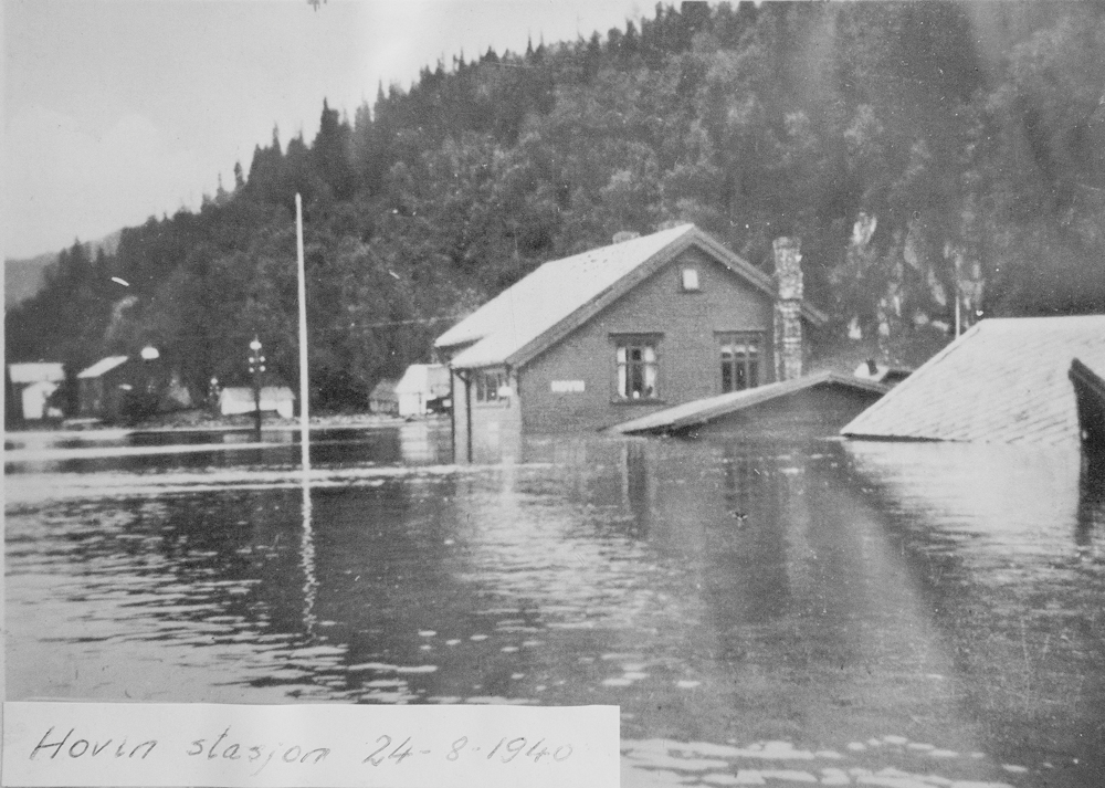 På det gamle bildet ses stasjons-bygningen under den store flommen 29. august 1940. Da sto vannet godt over etasjeskillet på butikken og det var en krevende oppryd-ningsprosess. Men husene står her den dag i dag. Det sier vel litt om kvaliteten på trevirket de er bygget i.