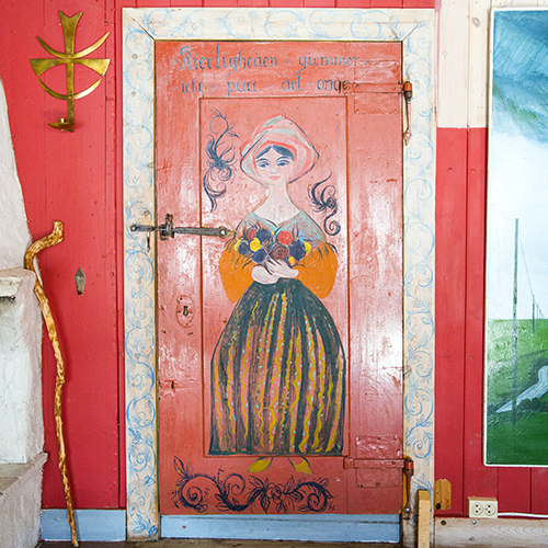 Ela forvandlet Thomasgården til et kunstverk. Hennes fargerike og livlige dekor er nesten overalt. På bildet ses motivet «Kiærligheten giemmer icke paa det onde»